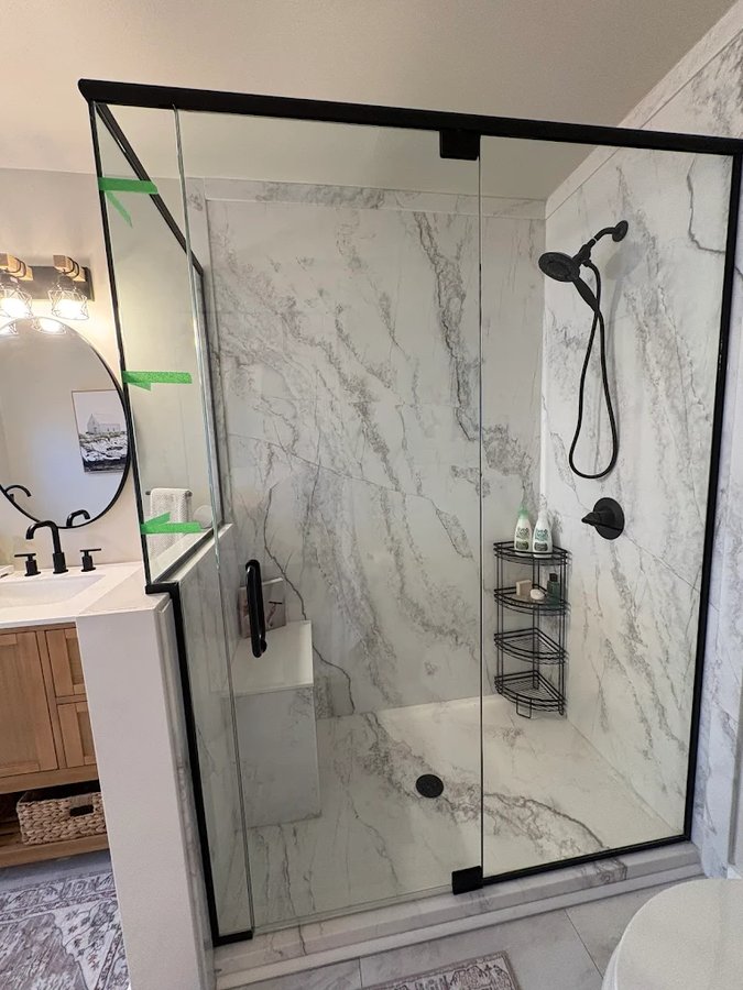 Walk-in shower with matte black frame, white marble walls, and rain plus handheld sprayer