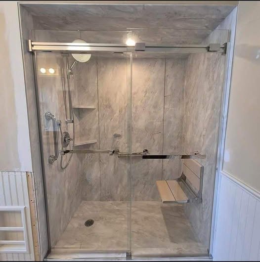 Walk-in shower with fold-down wood bench, grab bars, and grey marble-look walls