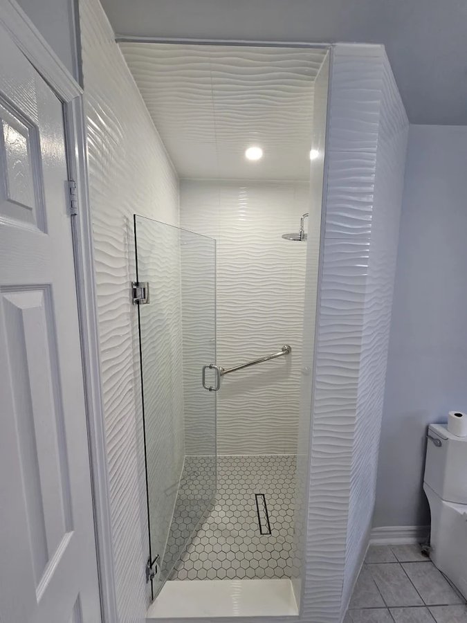 Compact walk-in shower with wave-textured white walls, hex mosaic floor, and linear drain