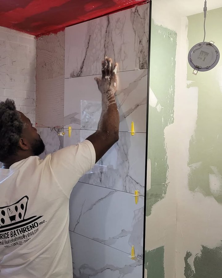 Maurice installing marble wall tile on a customer's bathroom renovation — wearing Maurice Bath Reno branded shirt